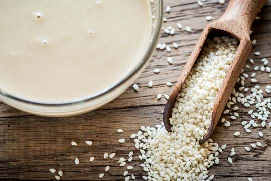 Bowl of techina next to a spoonful of sesame seeds